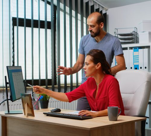 Team searching the best solution in front of computer in modern office room. Coworkers discussing working in workplace in personal corporate company typing on pc keyboard pointing at desktop