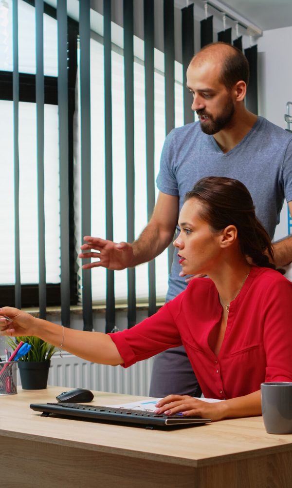 Team searching the best solution in front of computer in modern office room. Coworkers discussing working in workplace in personal corporate company typing on pc keyboard pointing at desktop